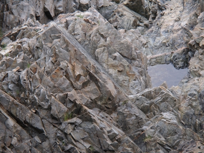 [Grey granite chipped and broken by water in its many forms. A small tidepool is visible.]